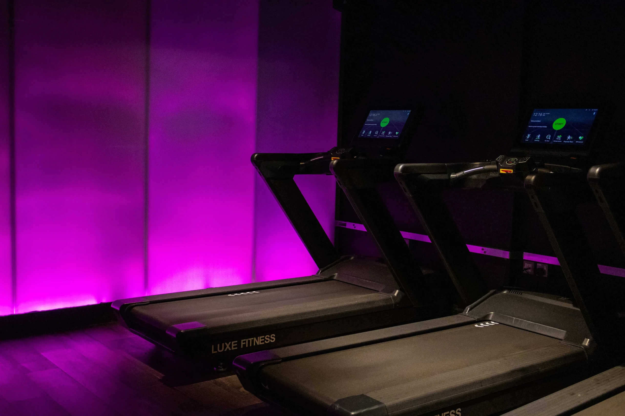 Luxe Fitness branded touchscreen treadmills illuminated by purple ambient lighting in Bristol gym