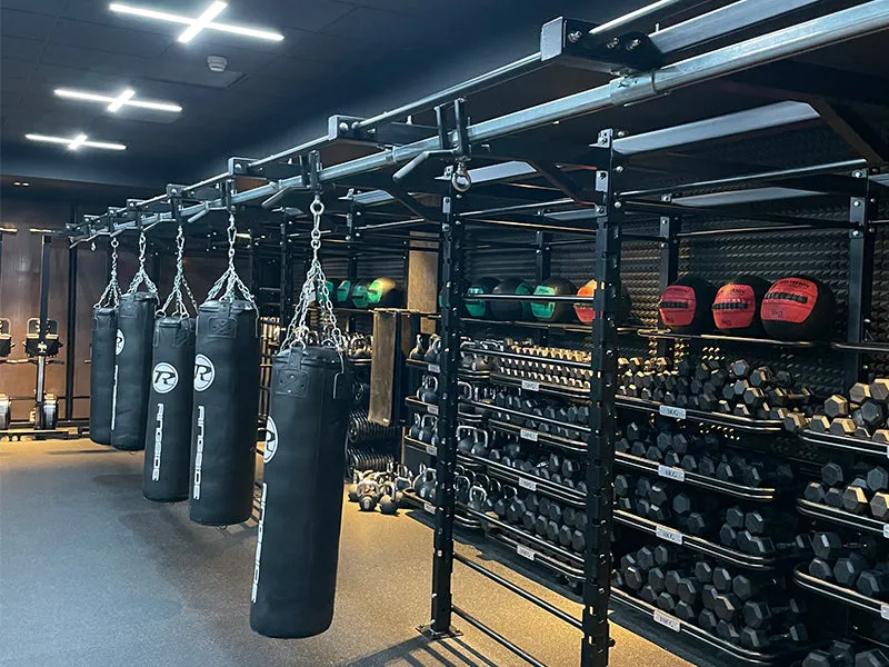 Multiple hanging punch bags positioned alongside an extensive dumbbell and medicine ball rack