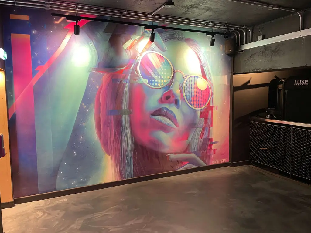 Wide view of colourful glitch-art mural and branded Luxe Fitness signage inside Bristol gym