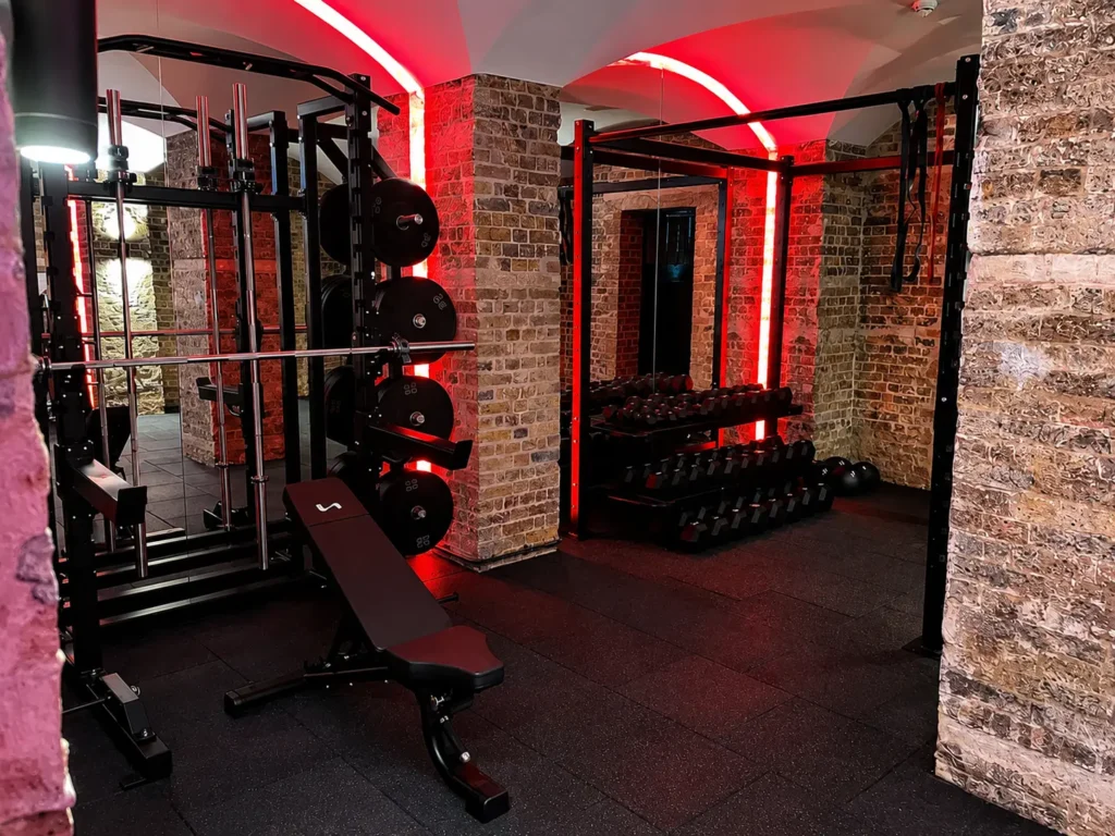 Weight rack and dumbbells inside exposed brick vaulted gym with red accent lighting