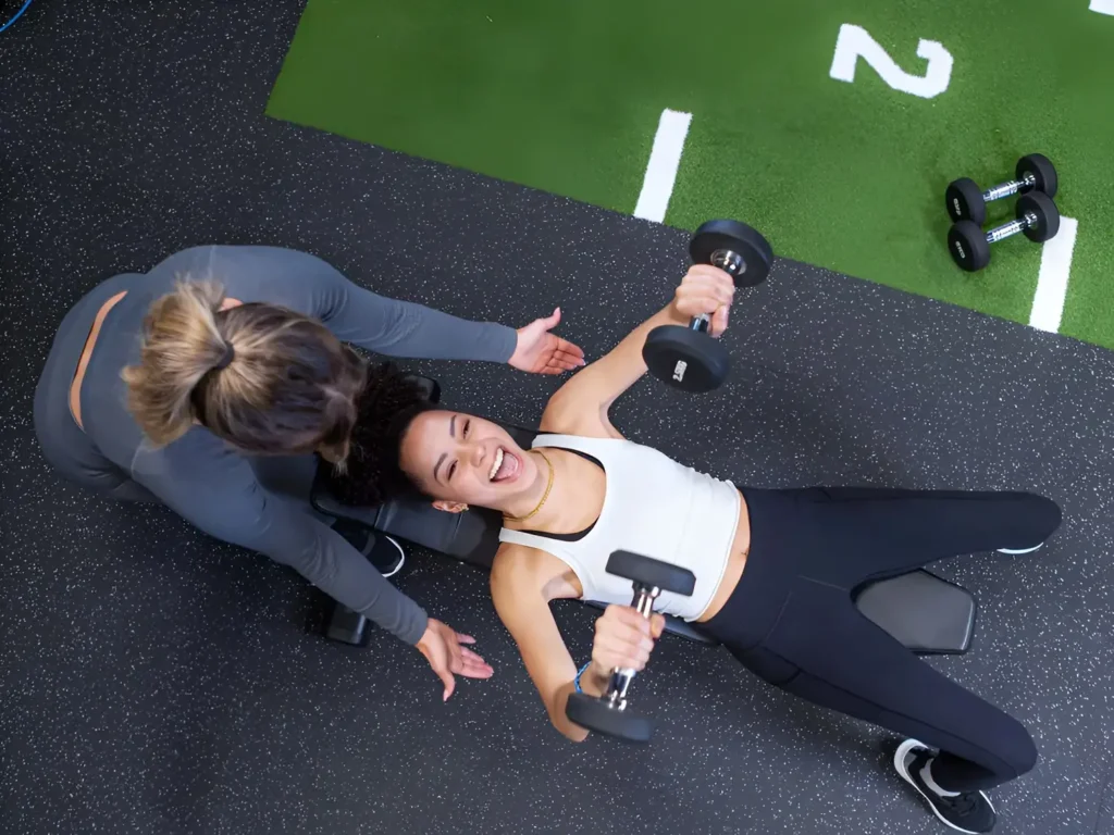 Overhead shot of a trainer coaching a woman through dumbbell bench press exercise