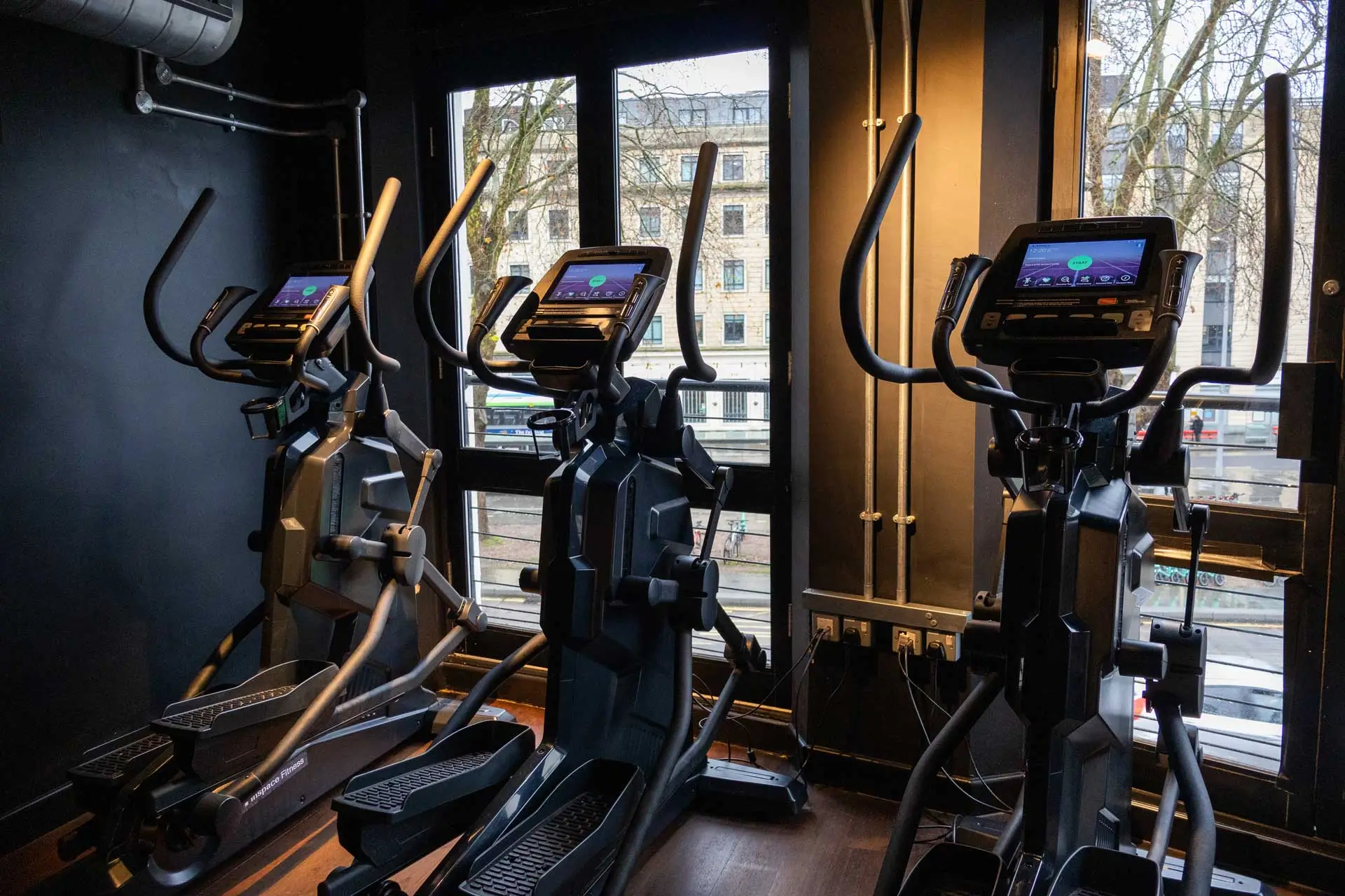Branded Inspace Fitness cross trainers positioned in front of large windows overlooking city street