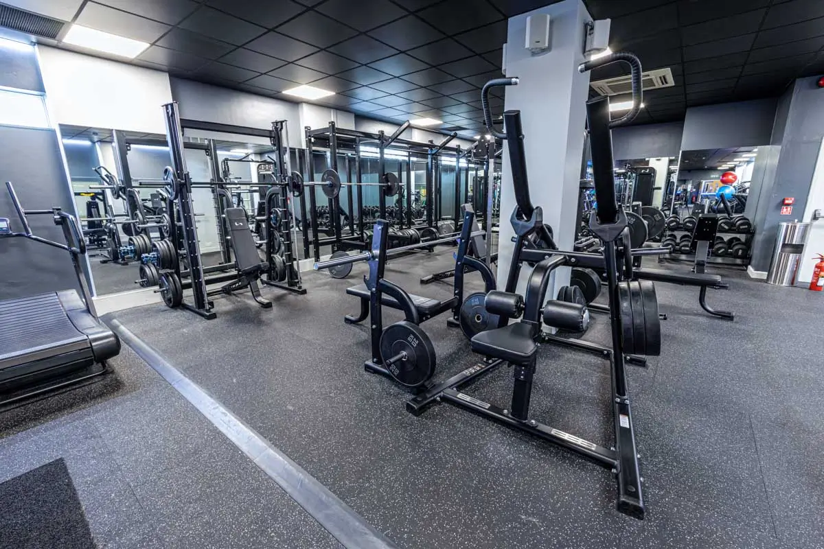 Strength equipment, benches, and squat racks arranged along a mirrored commercial gym wall
