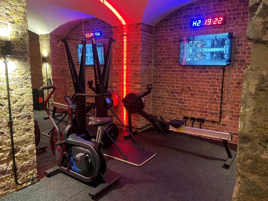Weight rack and dumbbells inside exposed brick vaulted gym with red accent lighting