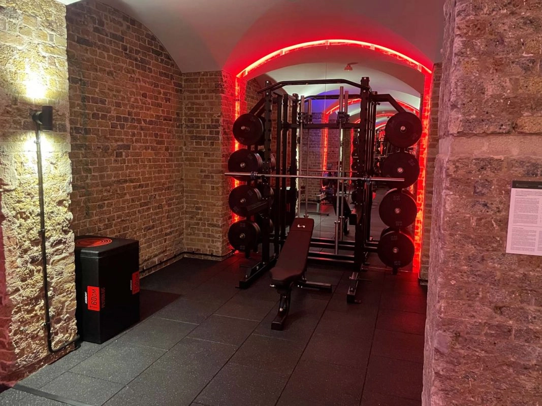 Weight rack and dumbbells inside exposed brick vaulted gym with red accent lighting