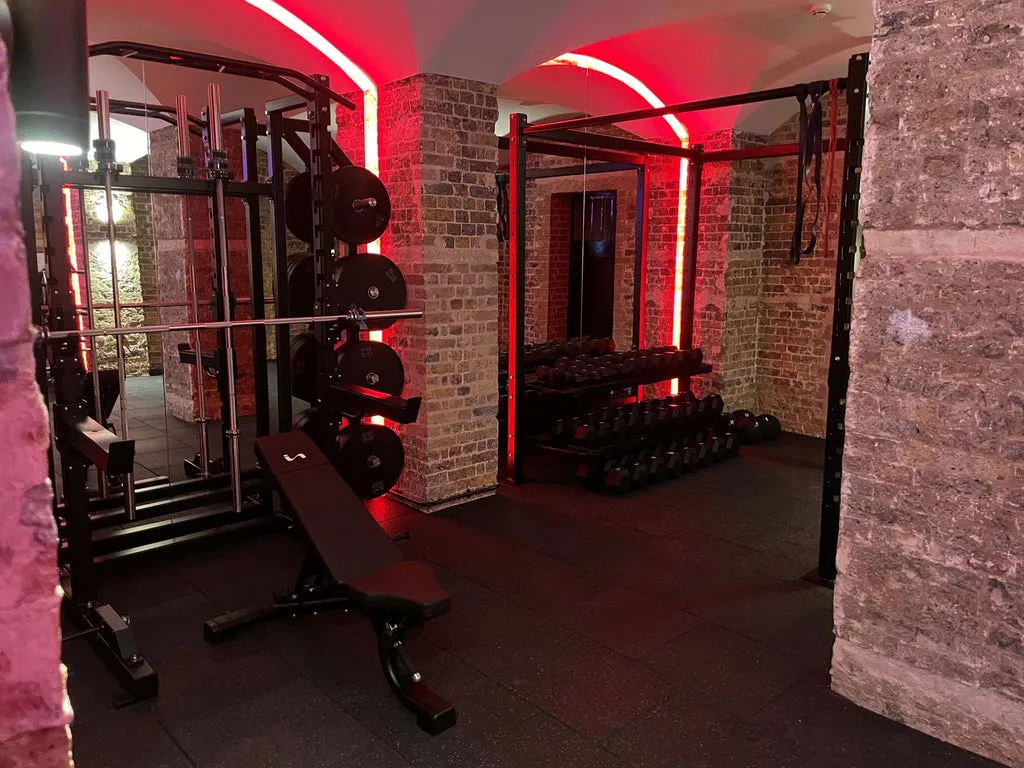 Weight rack and dumbbells inside exposed brick vaulted gym with red accent lighting